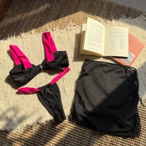Flat lay of a three-piece black and pink bikini set with matching mesh sarong skirt