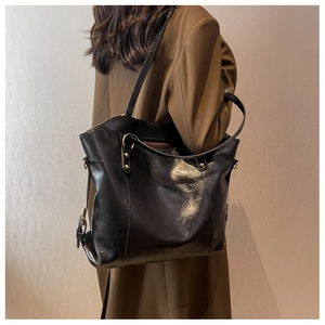 Detailed view of a black leather tote bag with oil wax finish worn by a model