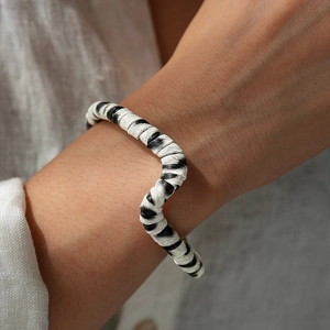 Detail of a wavy black and white striped leather bracelet on a model's wrist