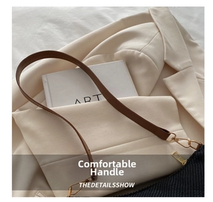 Detail view of brown leather handle and gold metal hooks on a minimalist black shoulder bag