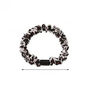 Detail of leopard print scrunchie showing glossy fabric texture and exact dimensions