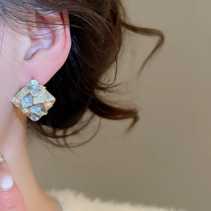 Close-up of geometric diamond-shaped earrings with mosaic inlay and gold plated edges