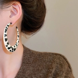 Close-up of a large C-shaped earring with black and white cow print worn by a model