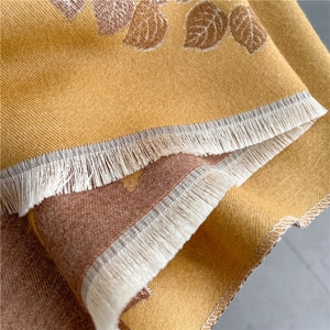 Close-up of yellow-brown jacquard scarf with leaf patterns and white fringe details
