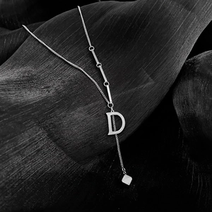 Minimalist silver letter D pendant necklace with bar link chain on dark leaf background