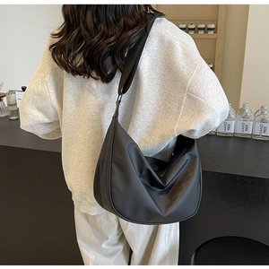 Detailed view of a black nylon crescent bag worn crossbody in a minimalist indoor setting
