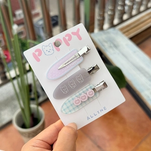 Close-up of three colorful hair clips featuring cat and apple patterns on a display card