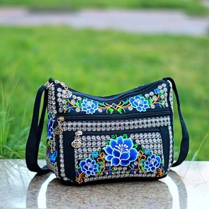Detailed close-up of ethnic floral embroidery on black canvas crossbody bag outdoors
