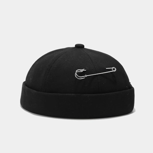 Detail of a black docker cap with a large silver safety pin and durable cotton texture