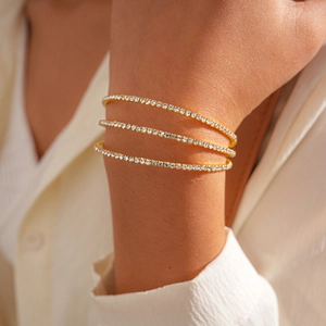 Close-up of three-layer gold bracelets with shimmering white zircons on a model's wrist