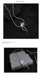 Detailed views of silver bow pendant necklace on textured black sand background