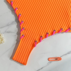 Detail of orange ribbed swimwear with pink side lace-up ties and silver metal eyelets