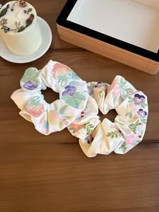 Detail shot of two white satin scrunchies with colorful floral embroidery on a wood surface