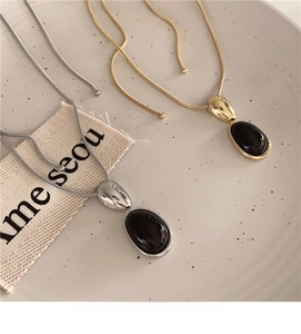 Detail of oval black resin pendant necklace in gold and silver finish snake chains