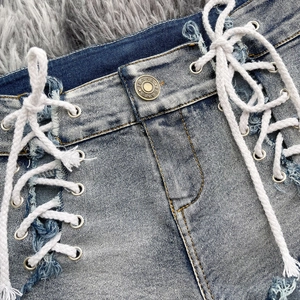 Dettaglio degli shorts in denim lavaggio blu con stringhe bianche laterali e occhielli in metallo