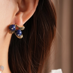 Macro shot of vintage gold floral earring with deep blue beads on ear, elegant jewelry set