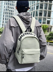 Detail of light green waterproof nylon backpack featuring black MUMU print and front pocket