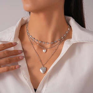 Detailed view of triple-layered silver necklace with pearl and vintage heart locket charms