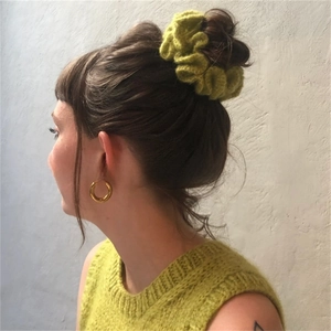Detail of green crochet ruffled hair scrunchie worn on a ponytail with knitted texture