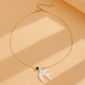 Détail du collier pendentif oiseau avec perle verte et chaîne dorée sur fond orange chaud