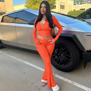 Orange two-piece lounge set with zip-up hoodie and flared trousers worn near a metal truck