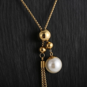 Dettaglio collana in metallo dorato con perla bianca grande e frangia con nappa