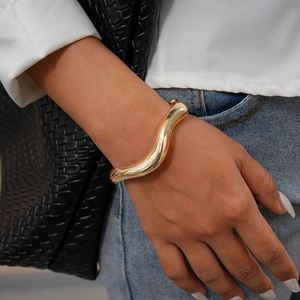 Detailed view of irregular golden wave bangle with polished finish on model wrist