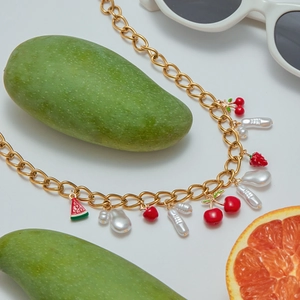 Detailed view of gold chain jewelry with pearl charms and red cherry fruit pendants