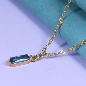 Close-up of golden necklace with blue rectangular zircon pendant on blue fabric