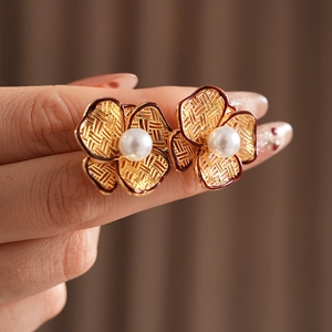 Close-up of gold flower stud earring with white pearl center and dark red petal edges
