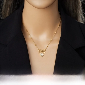 Détail du collier avec pendentif nœud et cœur doré serti de zircons sur fond noir