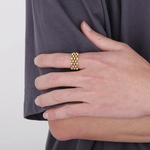 Detailed view of a gold watch strap style ring in stainless steel on a model hand