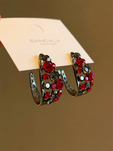 Détail rapproché des boucles d'oreilles en C avec zircons rouges et gris fumé