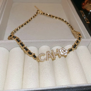 Close-up of pearl-embedded letters and camellia flower on a leather-wrapped chain