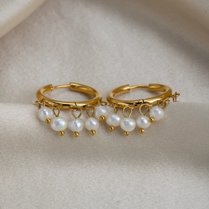 Macro shot of gold hoop earrings featuring five dangling white freshwater pearls on silk