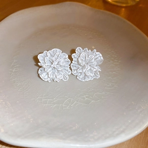 Detail view of elegant white layered flower stud earrings on white ceramic tray