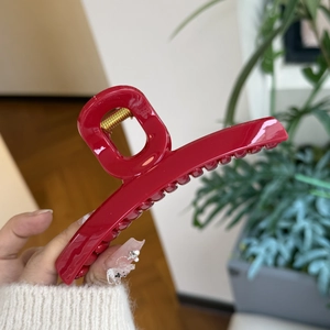 Detail of a large dark red resin claw clip with gold spring shown held by a hand