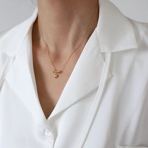 Close-up of a 18K gold-plated necklace featuring a 3D heart and bow pendant on a model