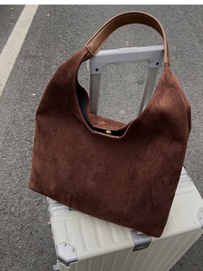 Detail of dark brown suede tote bag hanging on white suitcase handle against grey road