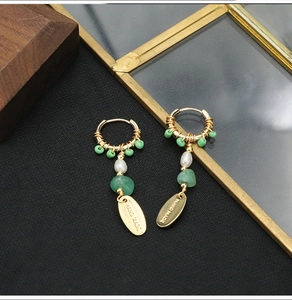 Detail of long drop earrings featuring green beads, freshwater pearls and gold charms