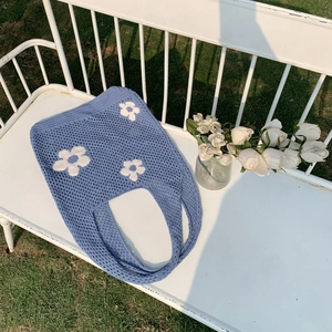 Detail einer hellblauen Stricktasche mit weißen Gänseblümchen auf einer Gartenbank