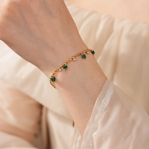 Détail d'un bracelet doré avec des breloques en malachite verte et des pierres en zircone