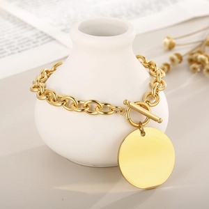 Close-up of golden stainless steel toggle bracelet with a polished blank round charm