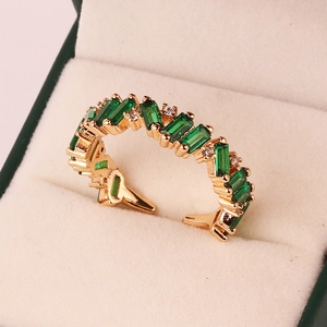 Macro detail of golden open ring with green baguette stones and white round crystals