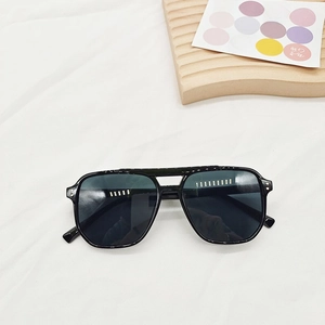 Square aviator sunglasses with black frame and gold rivet details on white fabric