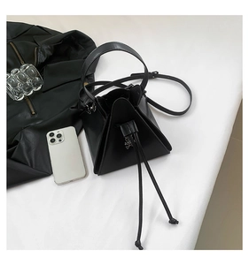 Detail view of a black geometric crossbody bag with a drawstring closure and smooth texture