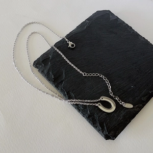 Detail of silver U-shaped horseshoe pendant with S.STEEL hallmark on black slate