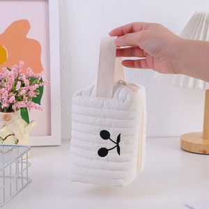 Detail der weißen gesteppten Kosmetiktasche mit Kirschstickerei und Reißverschlussgriff