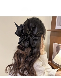 Detail of a large black satin tiered bow hair claw clip styled on a woman's half-up hair