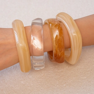 Nahaufnahme von vier dicken Harzarmbändern in Creme, Transparent und Bernstein am Arm